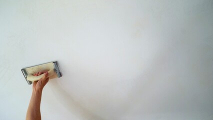 The final stage of sanding the ceiling, close-up of a hand. Grouting the ceiling using sandpaper. A professional mason works at a construction site, polishing the ceiling.