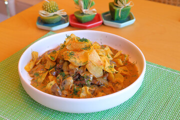 Stew with dried mushrooms and chips on a white plate.