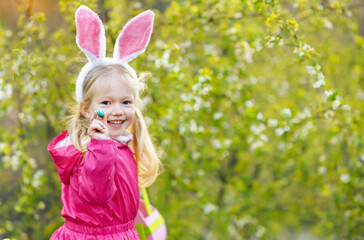Close up portrait of cute blond little girl with rabbit ears holding Easter egg in hand. Easter...