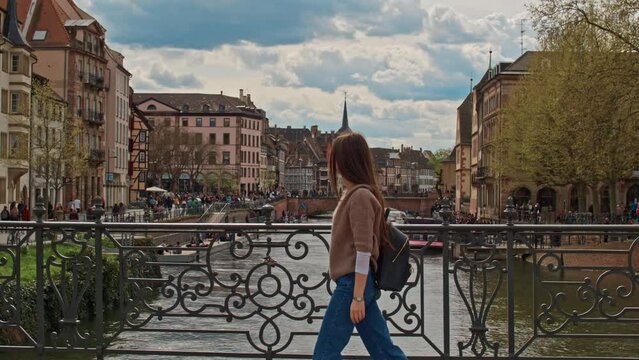 Tracking shot of young tourist woman walking along Strasbourg river bridge Petite France old french architecture buildings on a beautiful sunny day 