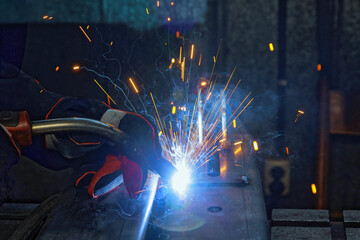 In factory, sparks are created as workers weld with gas argon to steel
