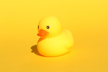 A yellow rubber duck stands on a yellow background.	