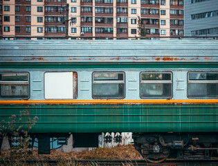 An old passenger railway car with peeling paint in the city on the background of houses and...