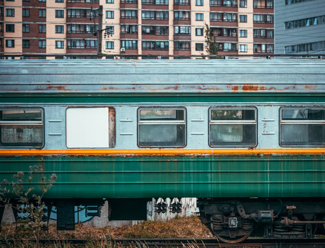 An old passenger railway car with peeling paint in the city on the background of houses and buildings. An empty carriage on the railway.