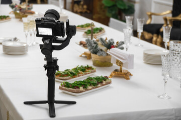 A stabilizer with a video camera on the table. buffet table with drinks and snacks. Selective...