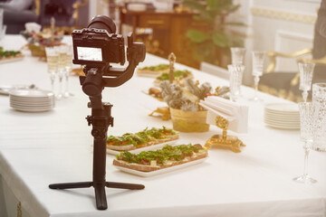 A stabilizer with a video camera on the table. buffet table with drinks and snacks. Selective...