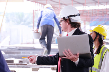 Engineer in safety helmet holding laptop working on job site.