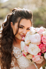 Naklejka premium Curly brunette bride poses with a bouquet, near a wooden railing. Magnificent dress with long sleeves, open bust. Spring wedding