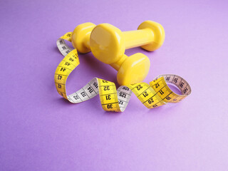 Yellow dumbbells with a measuring tape on a purple background