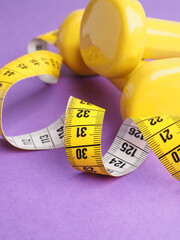 Yellow dumbbells with a measuring tape on a purple background