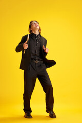 Young man, dressed smart casual, fashion and glasses outfit dancing of joy holding laptop against yellow background. Concept of work and education online, success in career development, betting. Ad