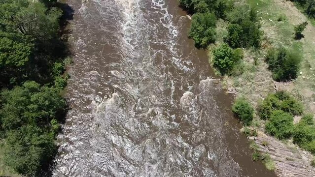 Rushing river seen from above and filmed with a drone. Aerial view of a mighty and swollen river in the Sierras of C&oacute;rdoba, Argentina. Brown mountain river with rushing water from the rains.