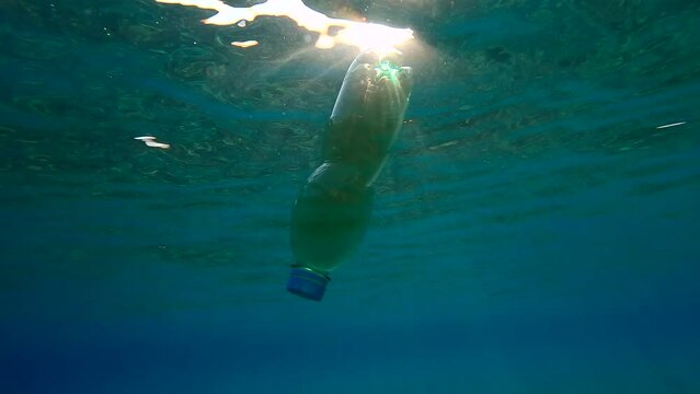 Closed plastic bottle with a drink drifts under surface of above sandy shallows water in sun rays, Backlighting, Slow motion, Plastic pollution of the Ocean