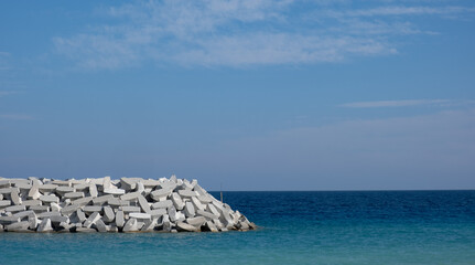 Fototapeta na wymiar Sea breakwater with cement blocks. Marine infrastructure. Blue calm sea and sky