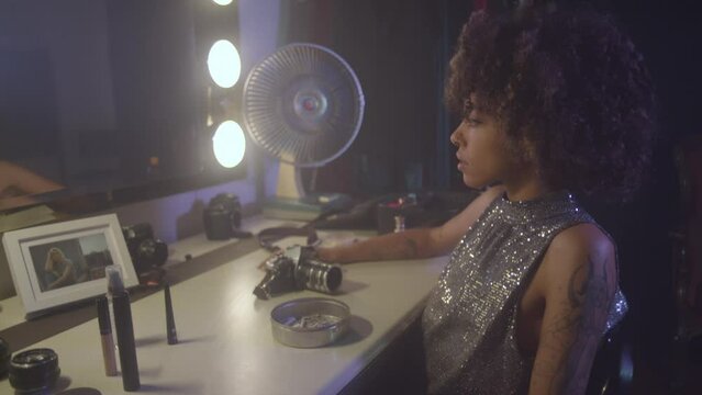 Afroamerican young woman tasting a cigarette in front of an old fashioned mirror, wearing a glitter dress.