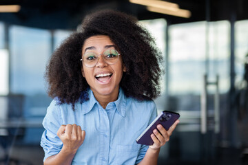 Close-up portrait of a young African-American woman working in the office, holding a phone and...