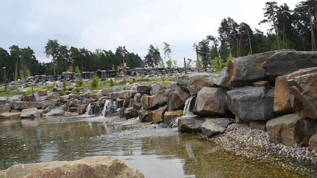artificial waterfall, stones, pine trees in cloudy weather in summer. Odintsovo district, Moscow region, Russia, Malevich Park is a modern park area that combines outdoor recreation, art and sports.