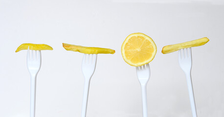 Diet concept, row of greasy french fries on plastic forks and a slice of lemon. Junkfood versus...