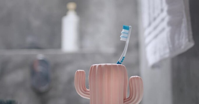 Male hand putting toothbrush in cup. Man put brush in toothbrush cup in shape of cactus on background of gray bathroom. Protection against caries dental calculus tartar, prevention of dental diseases.
