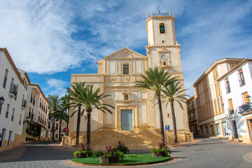 View of the 18th century Basilica Santa Maria de La Nucia dedicated to the Immaculate Conception with huge palm trees in front on Plaza Major in an old town center of La Nucia, Alicante