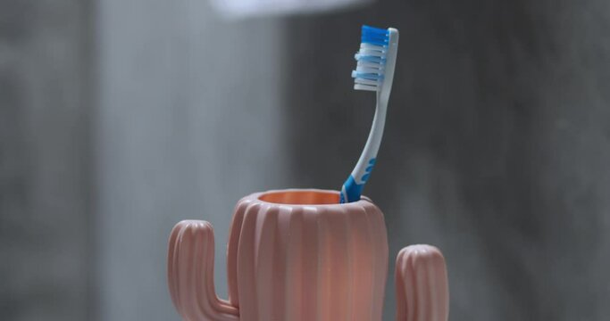 Male hand putting toothbrush in cup. Importance of daily brushing of teeth mouth to protect against tooth decay gums oral flora. Man putting brush in cup after brushing teeth in morning or evening
