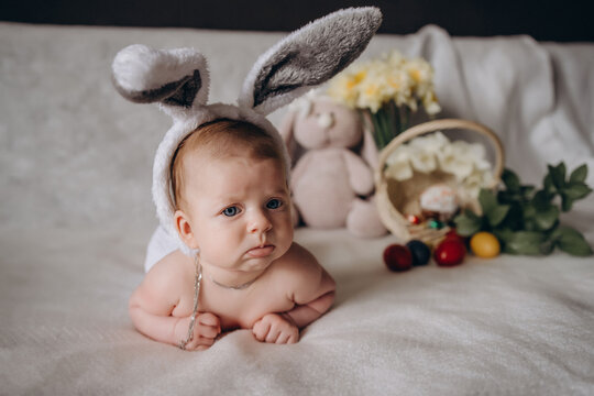 Cute little baby gets angry wearing bunny ears for Easter. Near Easter eggs.