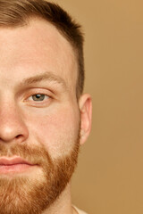 Obraz premium Half portrait of beautiful calm young man looking at camera. Male model serene and composed. Against beige background. Concept of beauty treatment, selfcare and hygiene, cosmetic, spa.