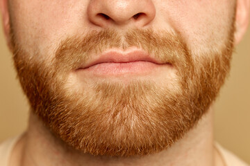 Obraz premium Cropped close up portrait of face young calm man with well kept skin and well-kept beard against beige studio background. Concept of beauty treatment, selfcare and hygiene, cosmetic, spa.