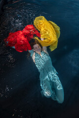 Young woman under surface of water swimming with yellow and red chiffon