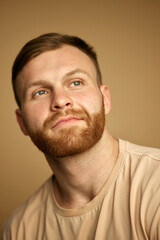 Fototapeta premium Portrait of young attractive shirtless man with red head and bear looking at camera against beige studio background. Concept of beauty treatment, selfcare and hygiene, cosmetic, spa. Ad
