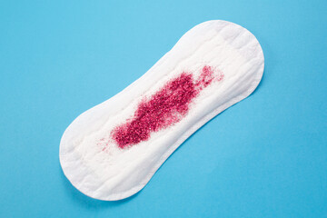 Feminine hygiene pad with red glitter on blue background. First menstrual period concept 