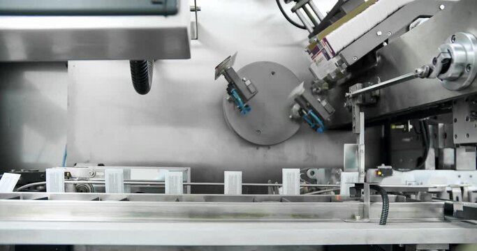 Manufacturing line at medical factory.Robotic arm put medicine package on conveyor belt.Packaged at automated production line. Packaging of drug. Medical factory assembly line packing medicine machine