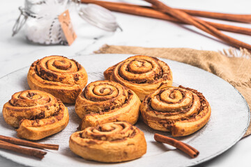 Homemade cinnamon rolls on white plate on white marble background