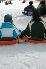 Young people sitting in sledges to go down the slope