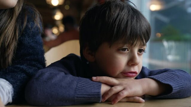Bored small boy complaining, sulking child feeling annoyed leaning on restaurant table, closeup kid face