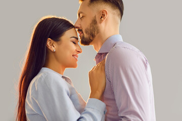 Portrait of a happy smiling affectionate young couple man and woman standing with closed eyes isolated on gray background and hugging. Care, love, tenderness and Valentines day concept.