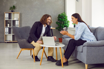 Young business people having meeting at office sitting on sofa and talking. Two workers smiling...