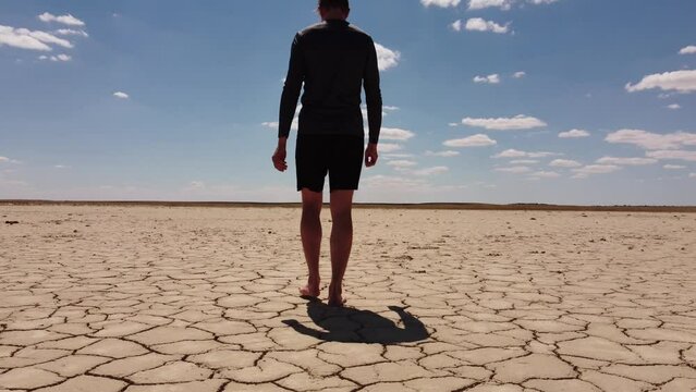 adult man walking barefoot on bottom of dried lake or river, drought concept, climate change