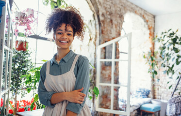 Young black woman wearing beige apron on flower shop background with copy space.
