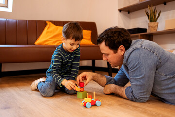 Happy young handsome father playing with little kid, son, with wooden blocks building