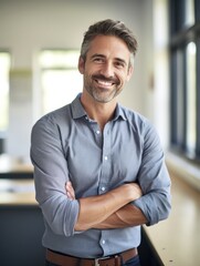 Naklejka premium smiling male teacher standing in classroom with arms crossed.