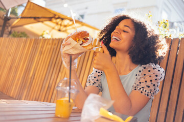 Young african american girl eating classic burger and drinking lemonade in the city