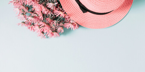Wicker hat, beautiful pink flowers chamomile on pastel blue background. Summer floral concept. Flat lay, top view, copy space, banner