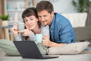 couple with coffees on the floor looking at a laptop
