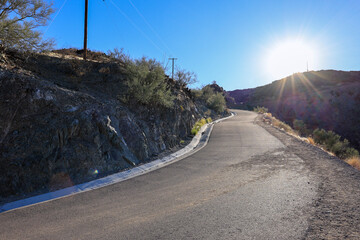 Backlit shot with star-shaped glare around sun of a paved service road that runs from the bottom to...