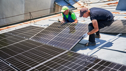 Workers building solar panel system on metal rooftop of house. Two men installers installing...