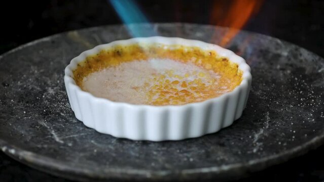 Burning cr&egrave;me br&ucirc;le&eacute; with a blowtorch. Caramelizing the sugar in the cr&egrave;me brule turning in white ramekins on a rustic wooden background