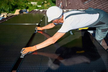 Worker building solar panel system on rooftop of house. Man engineer in helmet and gloves...