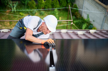 Worker building solar panel system on rooftop of house. Man engineer in helmet installing...