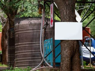 Pancarte blanche clouée sur un arbre avec en arrière plan des signalétique et une vielle citerne de réservoir à eau 